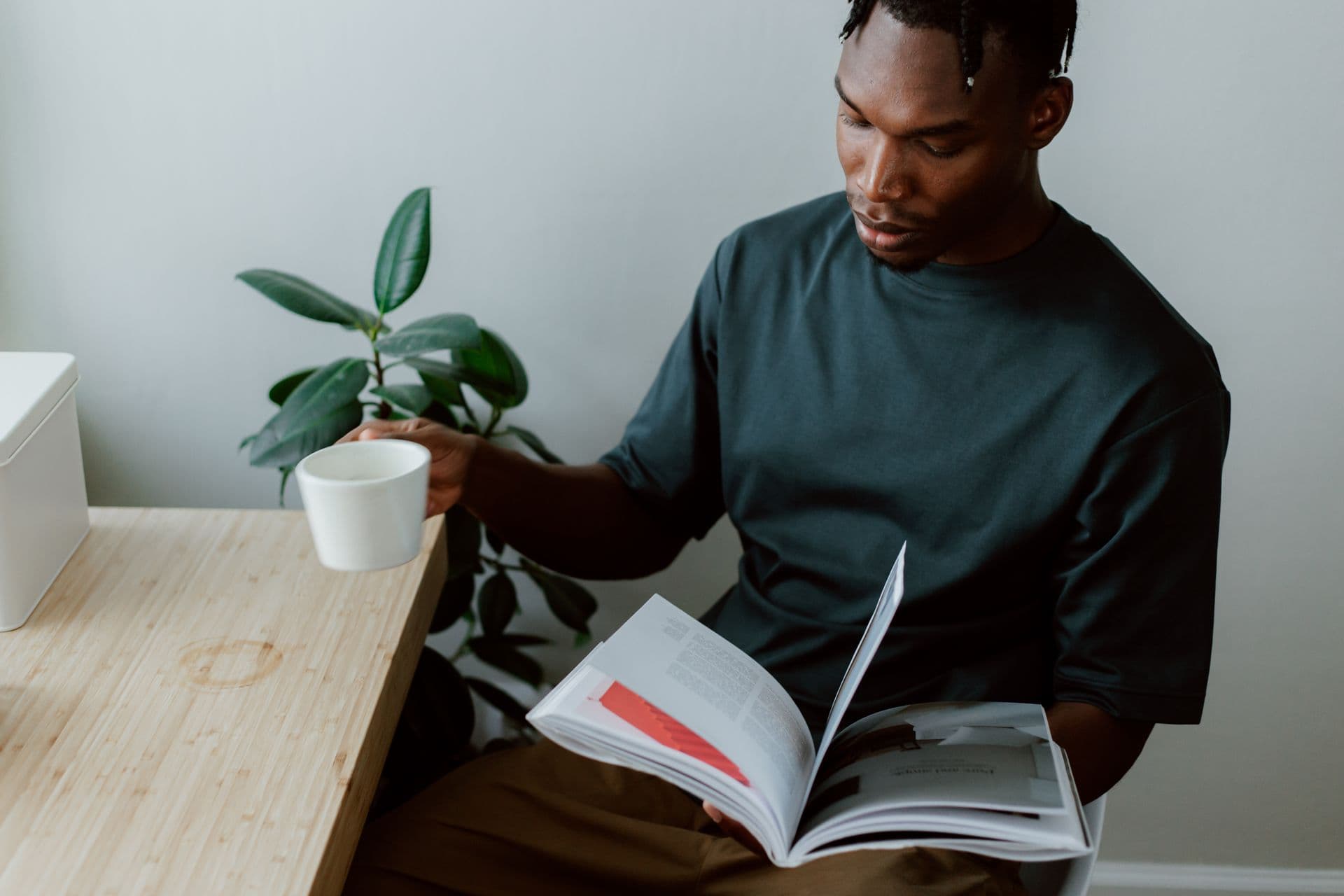 A reader turns the pages of a magazine at his desk, coffee beside him
