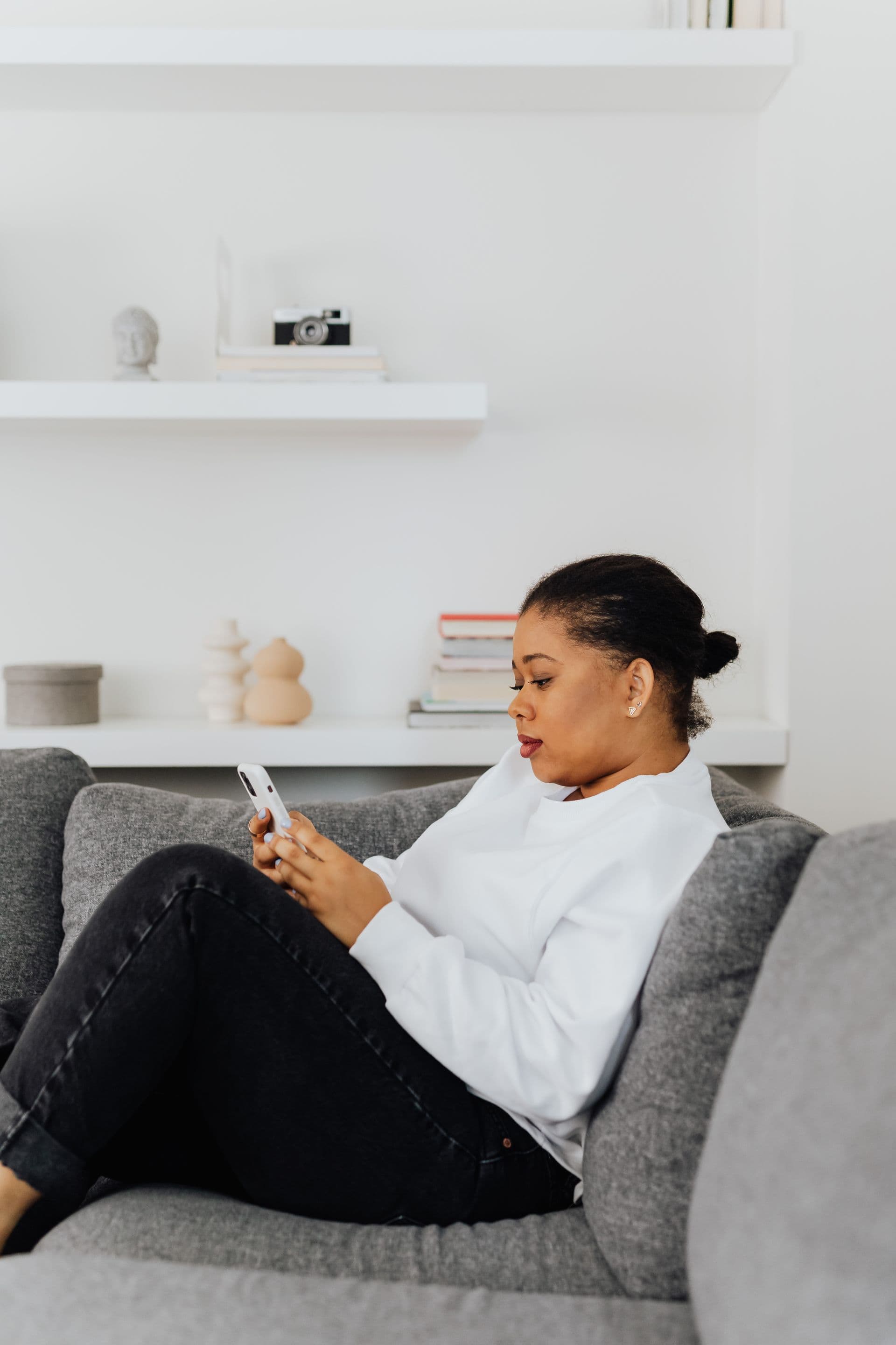 A reader relaxes on a grey sofa, reading on her phone