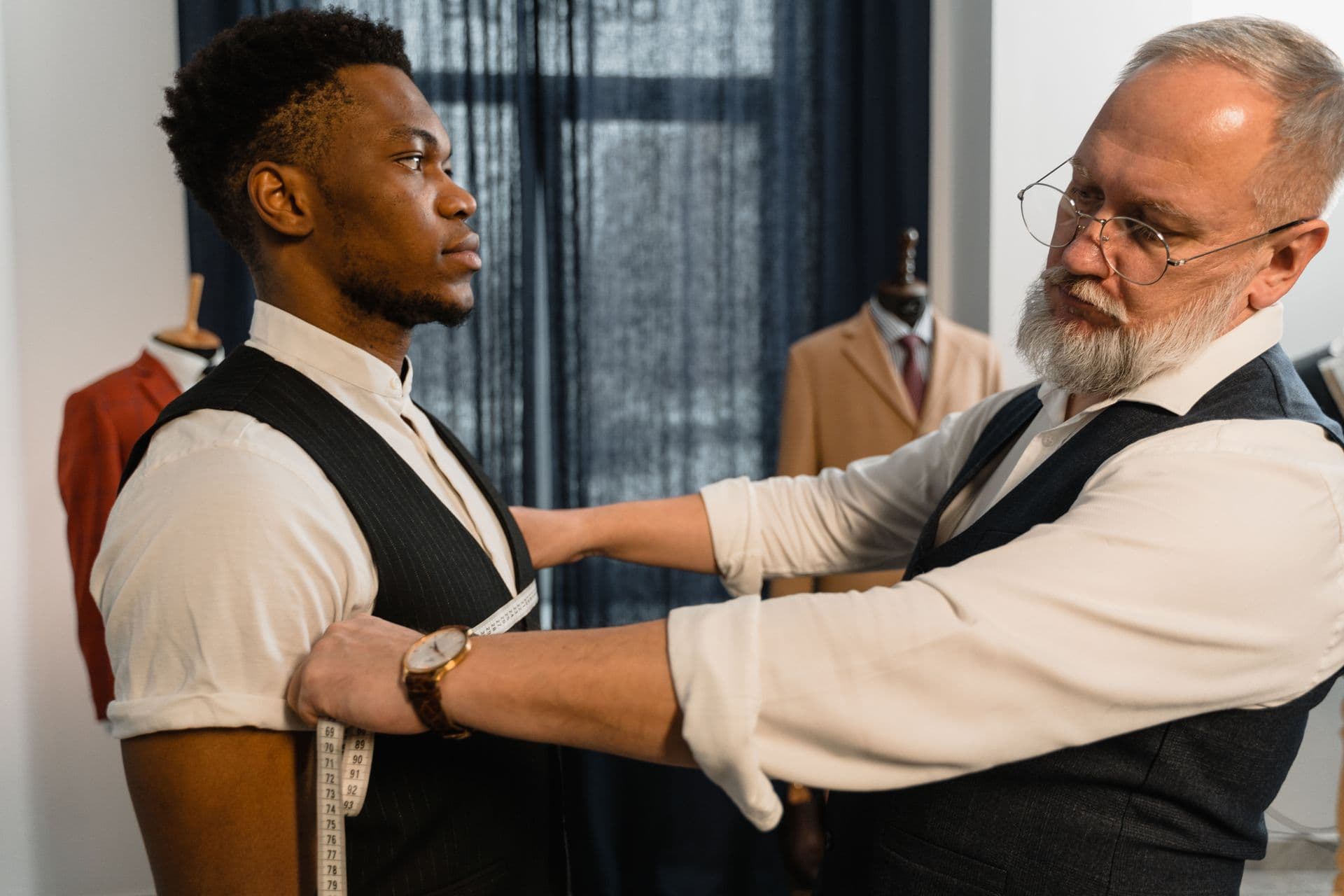 A tailor fits a client's waistcoat in a bespoke studio
