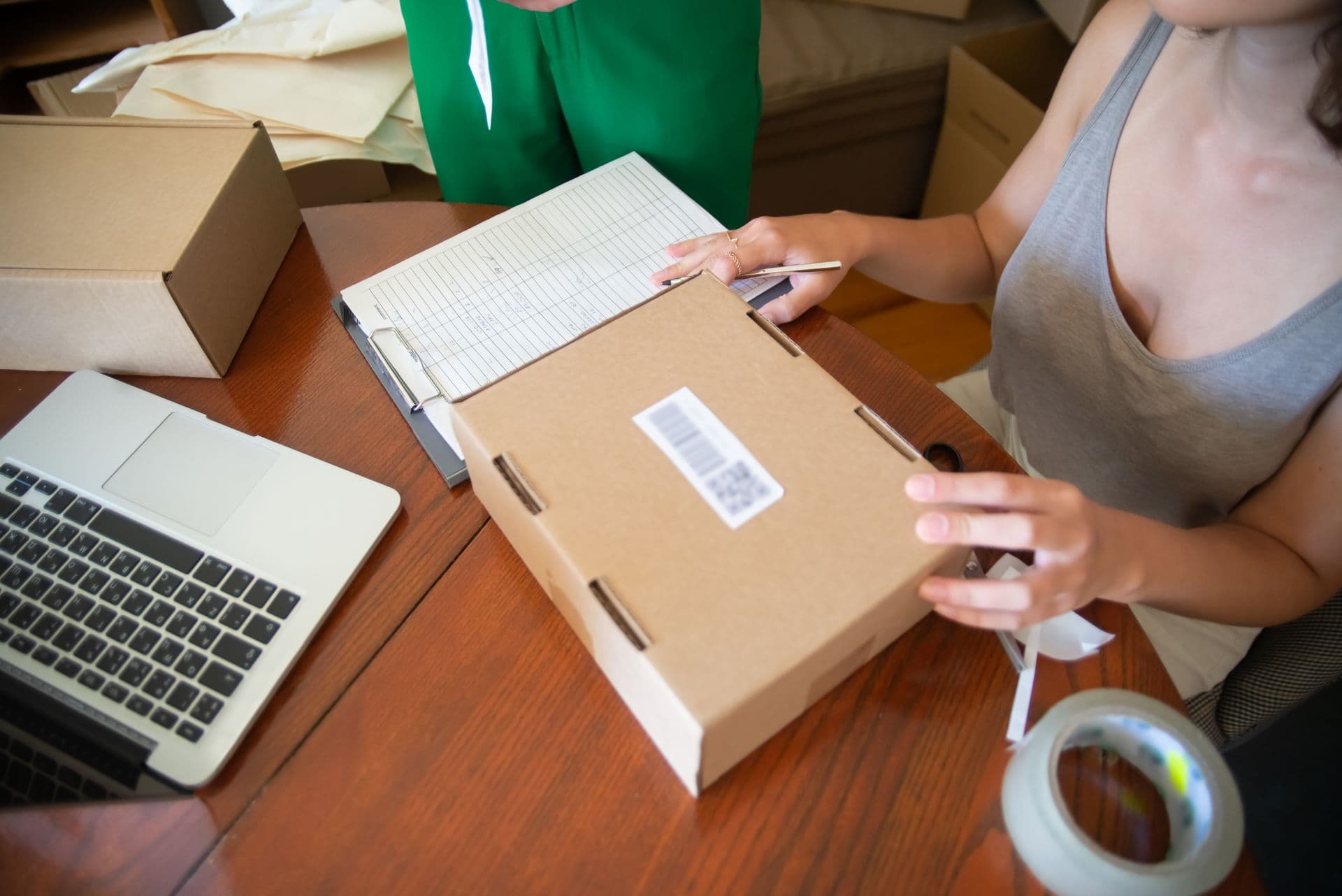 Hands seal a parcel with tape, an order slip beside it