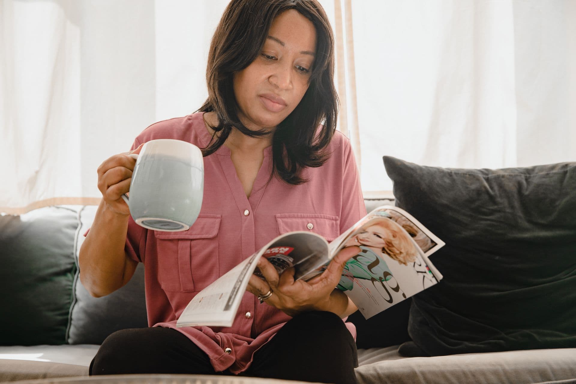 A reader on a sofa turns the pages of a magazine, a mug in her hand