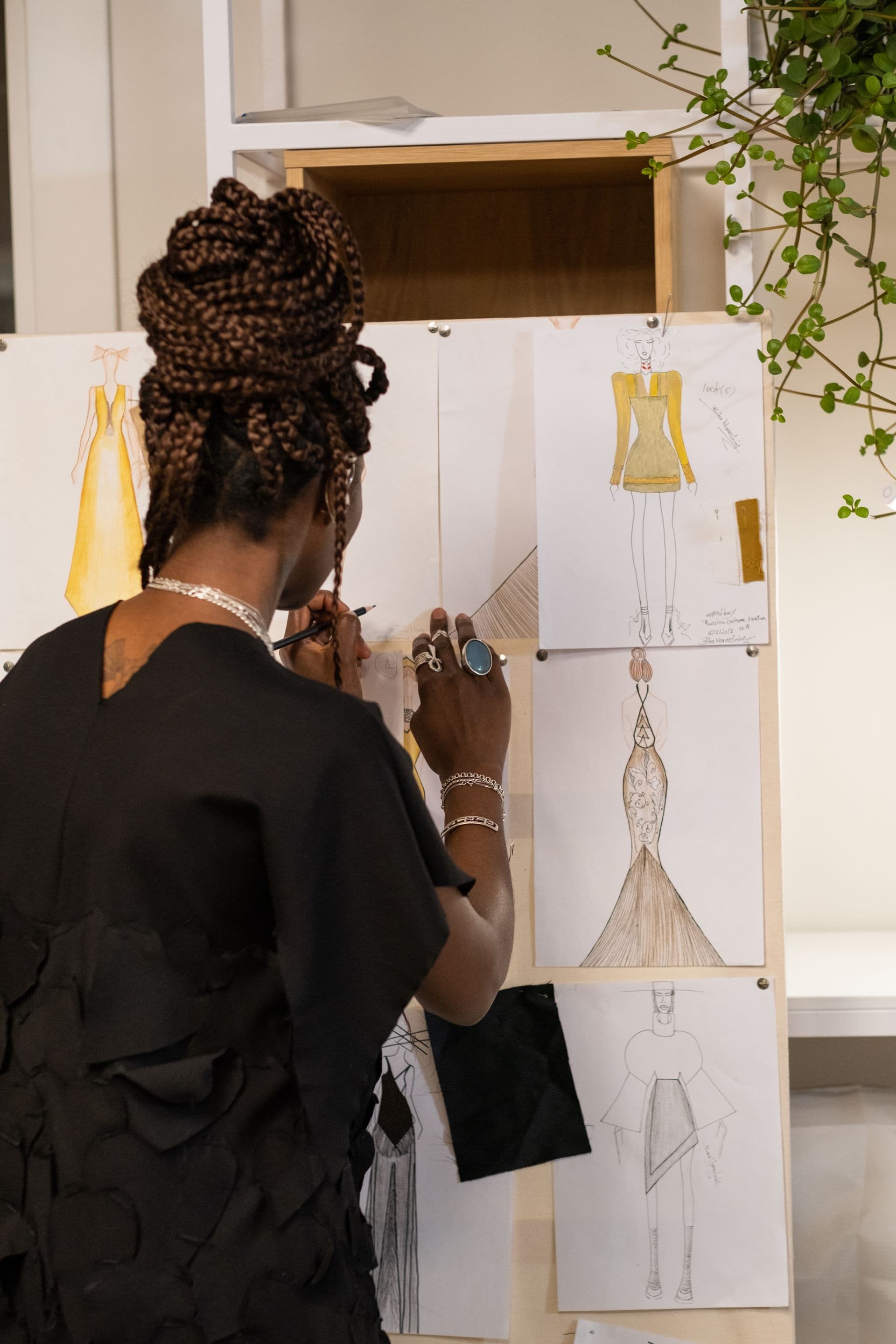 A designer pins dress sketches to a studio board