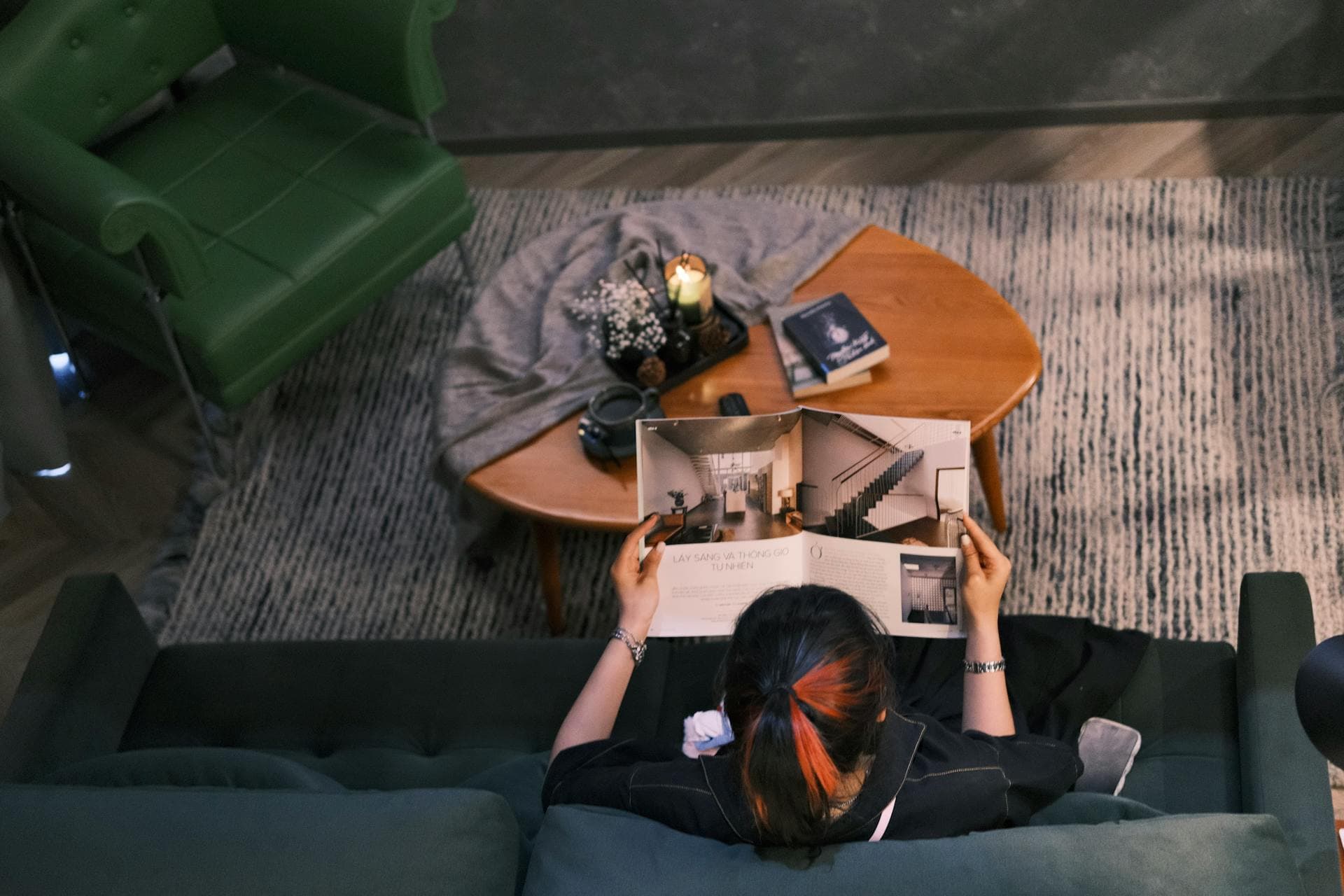 Reader on a velvet sofa holding open an architecture magazine beside a candlelit table