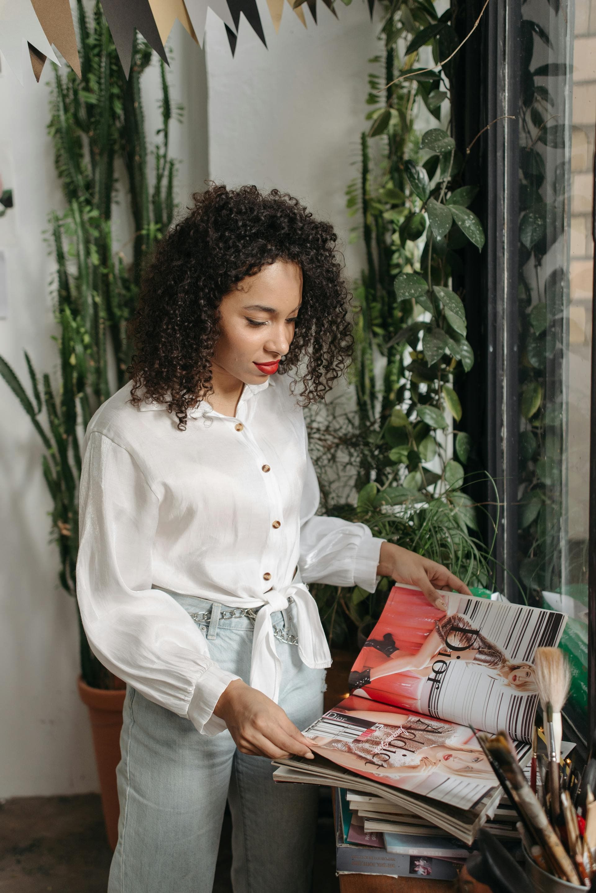 Editor browsing a stack of magazines in a plant-filled studio